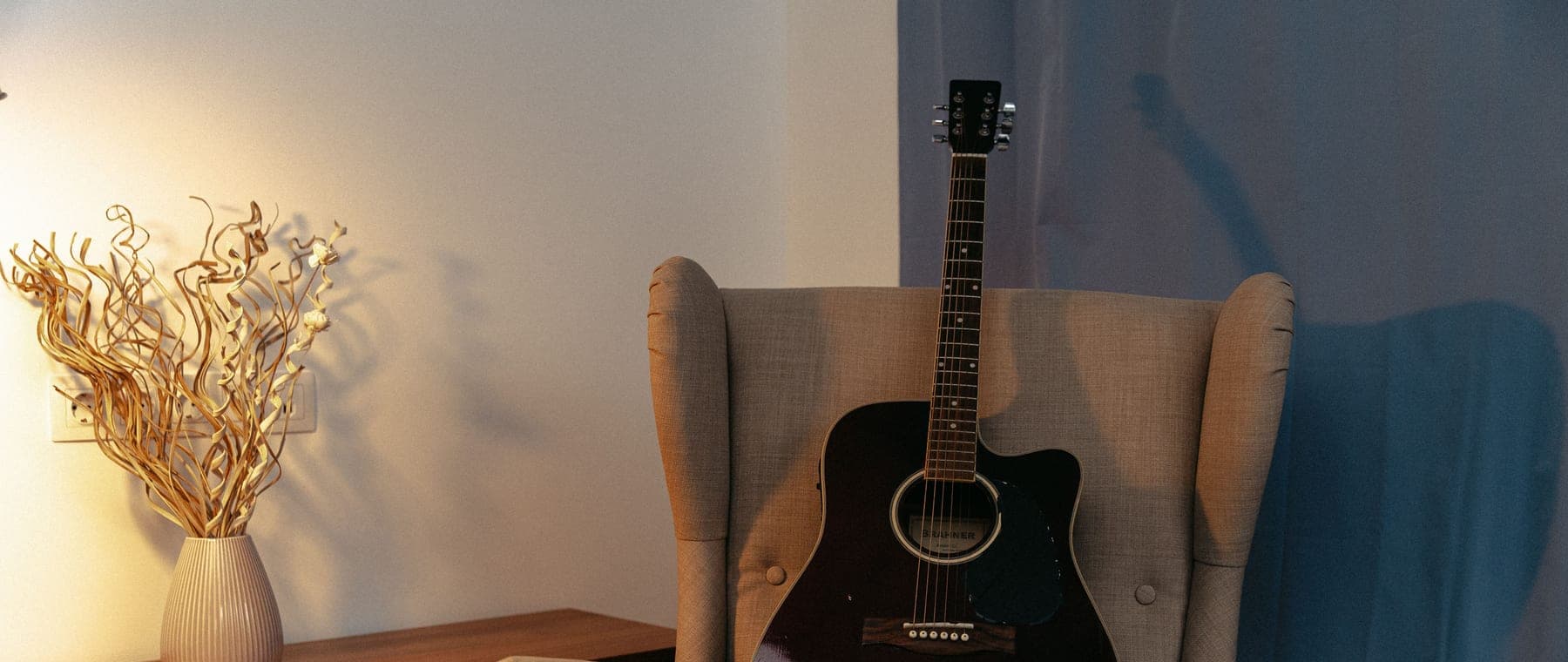 An acoustic guitar leaning against the wall of a warmly lit living room